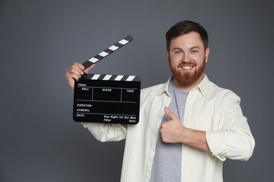 Making movie. Smiling man with clapperboard showing thumb up on grey background. Space for text