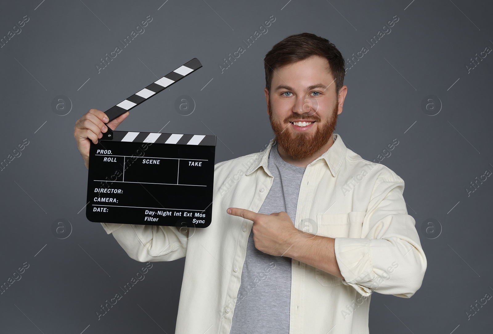 Photo of Making movie. Smiling man pointing at clapperboard on grey background