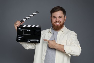 Making movie. Smiling man pointing at clapperboard on grey background