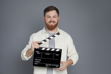 Photo of Making movie. Smiling man with clapperboard on grey background