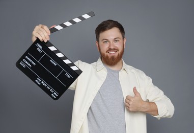 Making movie. Smiling man with clapperboard showing thumb up on grey background