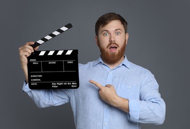 Making movie. Surprised man pointing at clapperboard on grey background