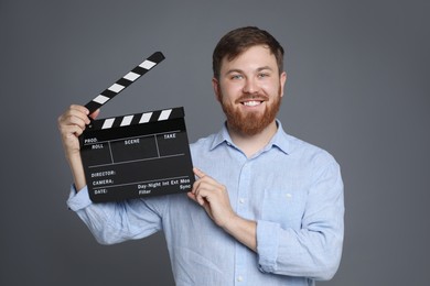 Making movie. Smiling man with clapperboard on grey background