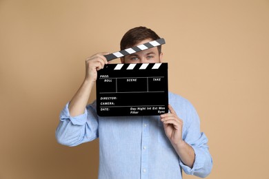 Making movie. Man with clapperboard on beige background