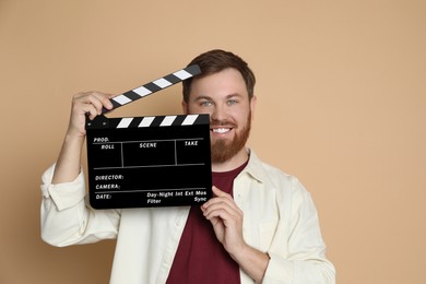 Photo of Making movie. Smiling man with clapperboard on beige background