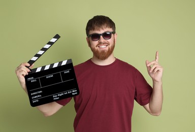 Making movie. Smiling man in sunglasses with clapperboard pointing at something on green background