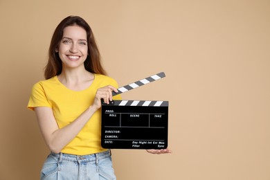 Photo of Making movie. Smiling woman with clapperboard on beige background. Space for text