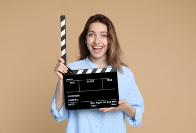 Making movie. Happy woman with clapperboard on beige background