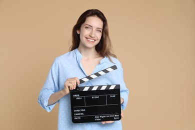 Making movie. Smiling woman with clapperboard on beige background