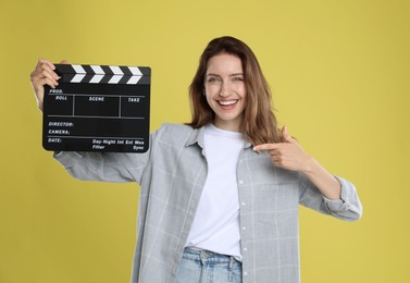 Photo of Making movie. Smiling woman pointing at clapperboard on yellow background