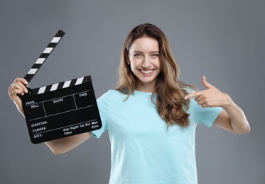 Photo of Making movie. Smiling woman pointing at clapperboard on grey background