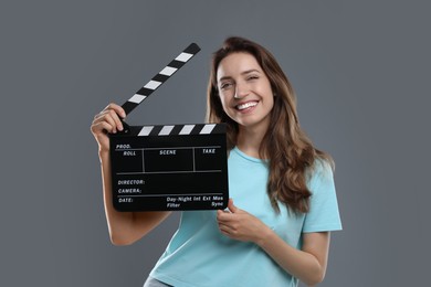 Making movie. Smiling woman with clapperboard on grey background