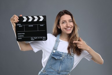 Photo of Making movie. Smiling woman pointing at clapperboard on grey background