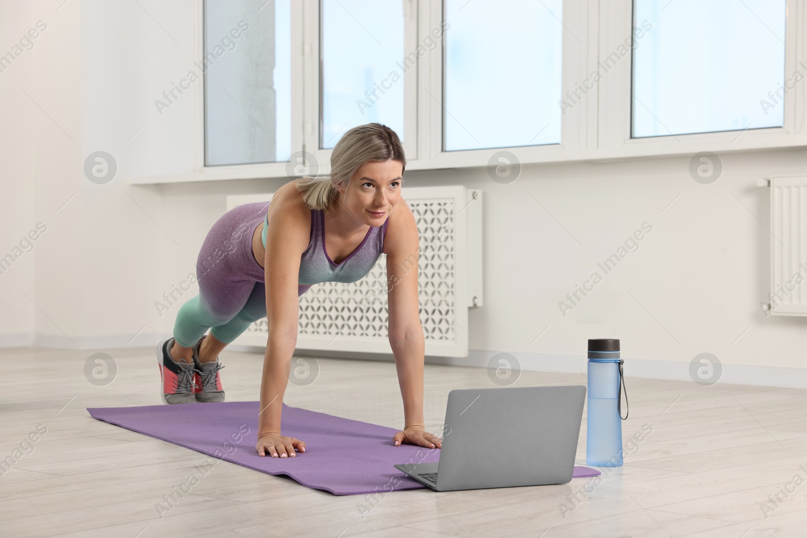 Photo of Online fitness trainer. Woman doing exercise near laptop at home