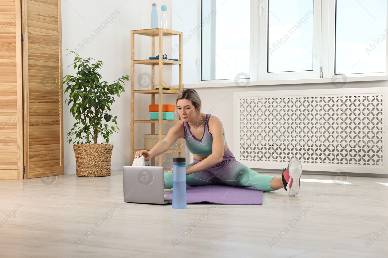 Photo of Online fitness trainer. Woman doing exercise near laptop at home