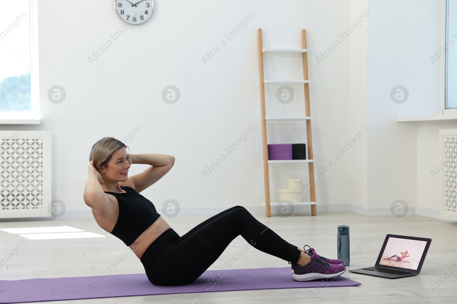 Photo of Online fitness trainer. Woman pumping up abs near laptop at home