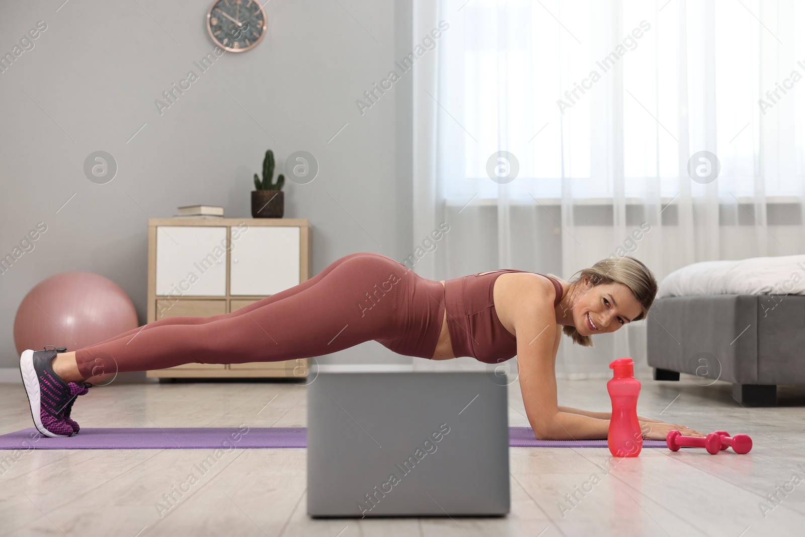 Photo of Online fitness trainer. Woman doing plank exercise near laptop at home