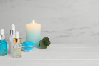 Aromatherapy products and burning candle on white wooden table, space for text