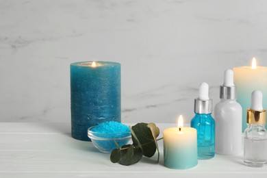 Aromatherapy products and burning candles on white wooden table