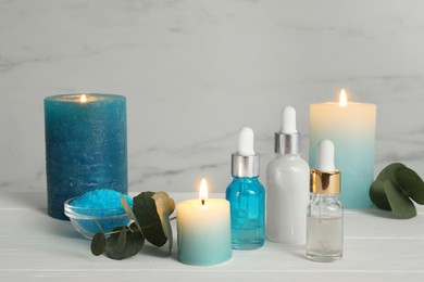 Photo of Aromatherapy products and burning candles on white wooden table