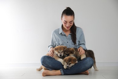Photo of Woman with Akita Inu puppies sitting on floor near light wall