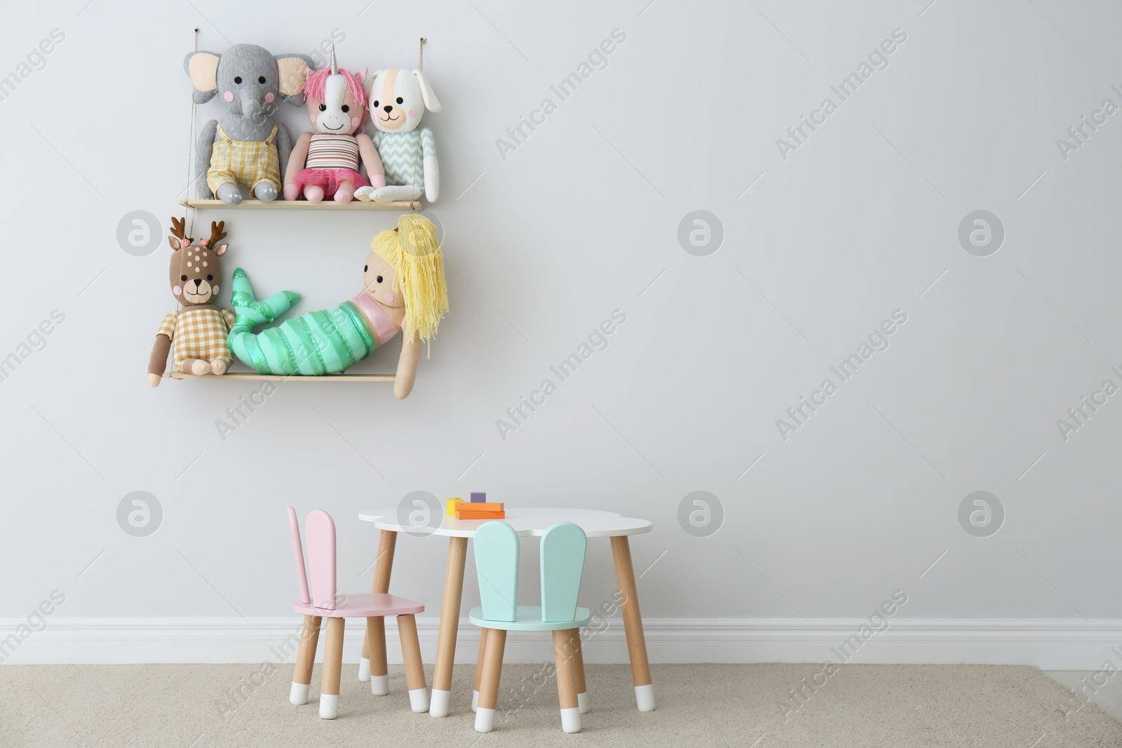 Photo of Table, chairs with bunny ears and collection of cute toys in child's room interior. Space for text