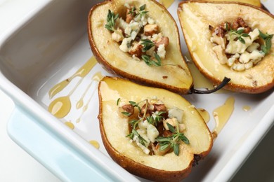 Photo of Tasty baked pears with nuts, blue cheese, thyme and honey in baking dish on table, closeup