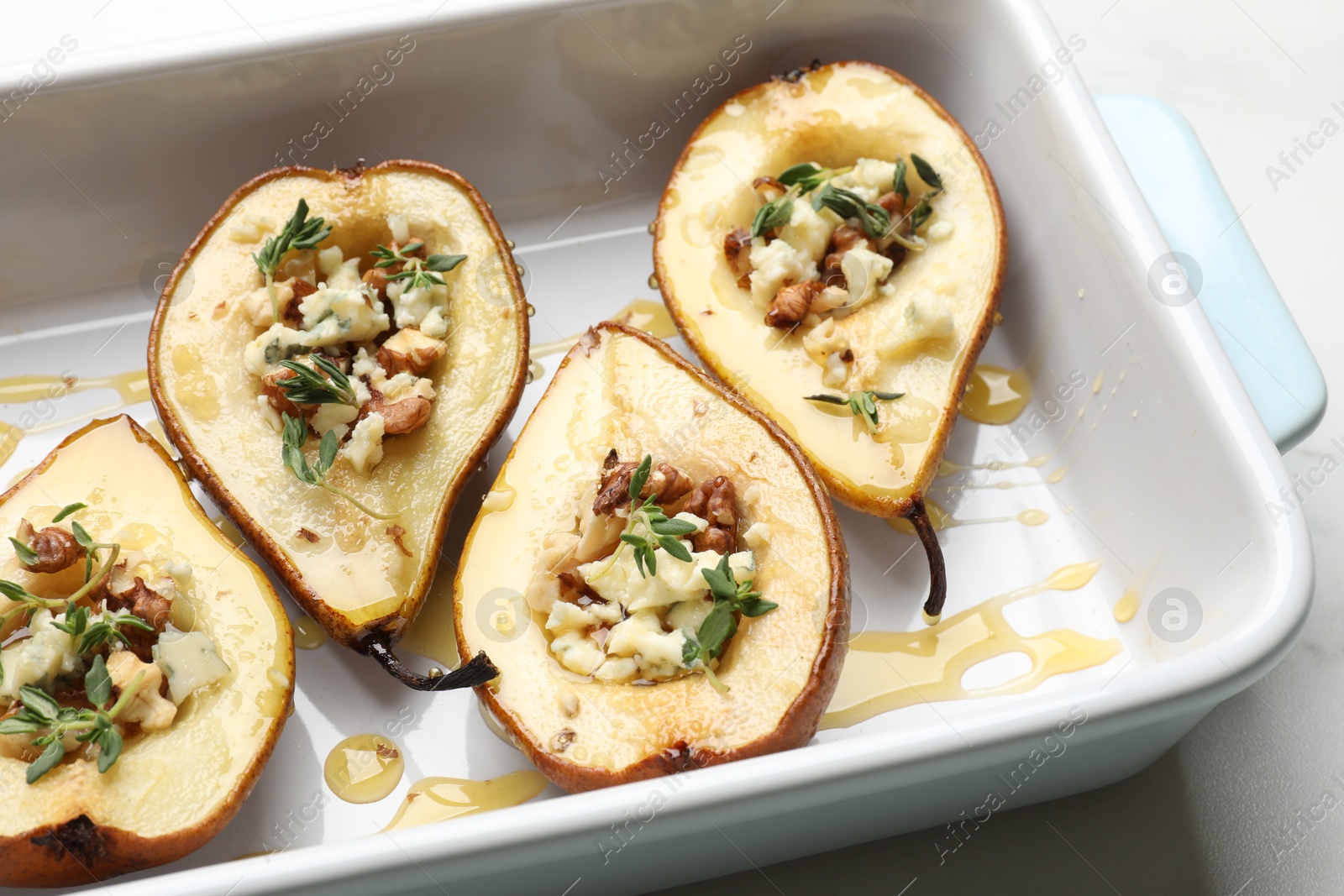 Photo of Tasty baked pears with nuts, blue cheese, thyme and honey in baking dish on table, closeup
