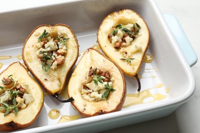 Tasty baked pears with nuts, blue cheese, thyme and honey in baking dish on table, closeup