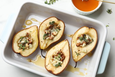 Photo of Tasty baked pears with nuts, blue cheese, thyme and honey in baking dish on table, flat lay