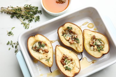 Photo of Tasty baked pears with nuts, blue cheese, thyme and honey in baking dish on table, flat lay