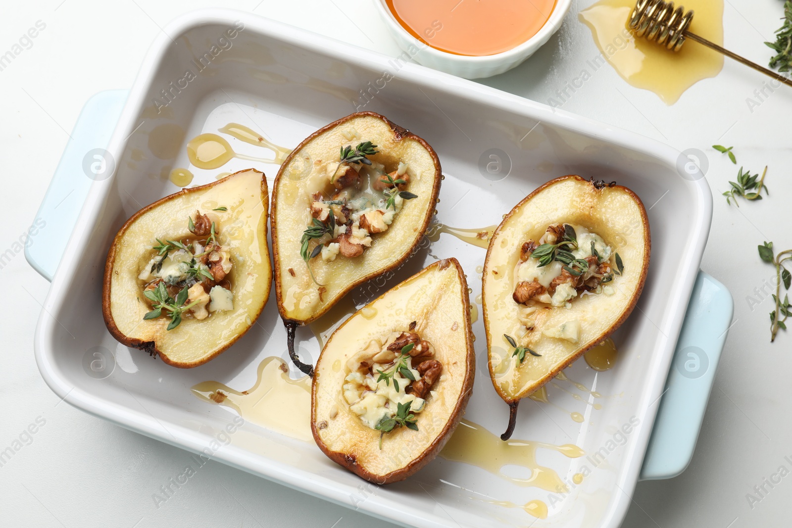 Photo of Tasty baked pears with nuts, blue cheese, thyme and honey in baking dish on table, flat lay