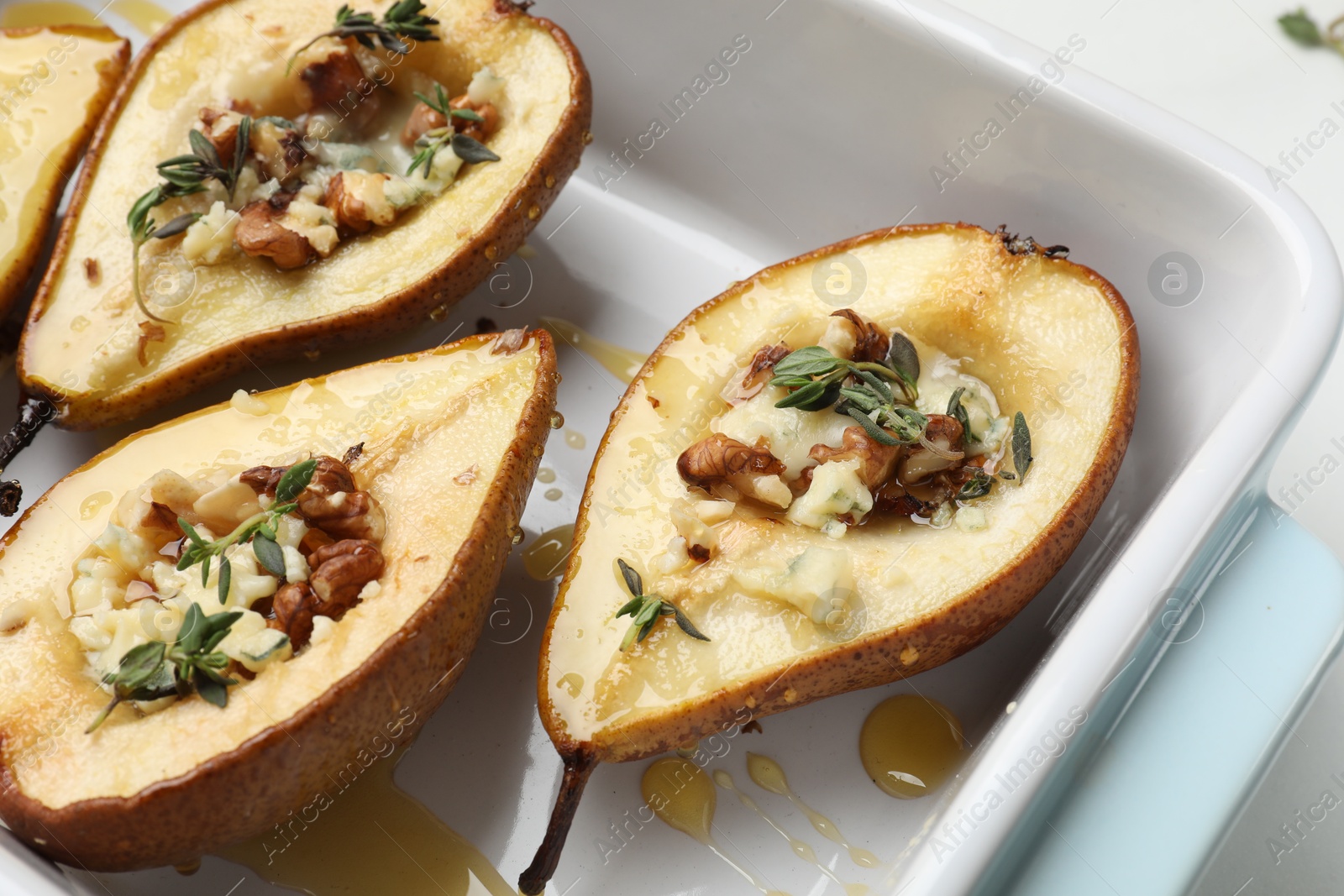 Photo of Tasty baked pears with nuts, blue cheese, thyme and honey in baking dish on table, closeup