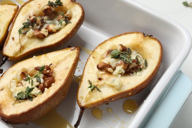 Tasty baked pears with nuts, blue cheese, thyme and honey in baking dish on table, closeup