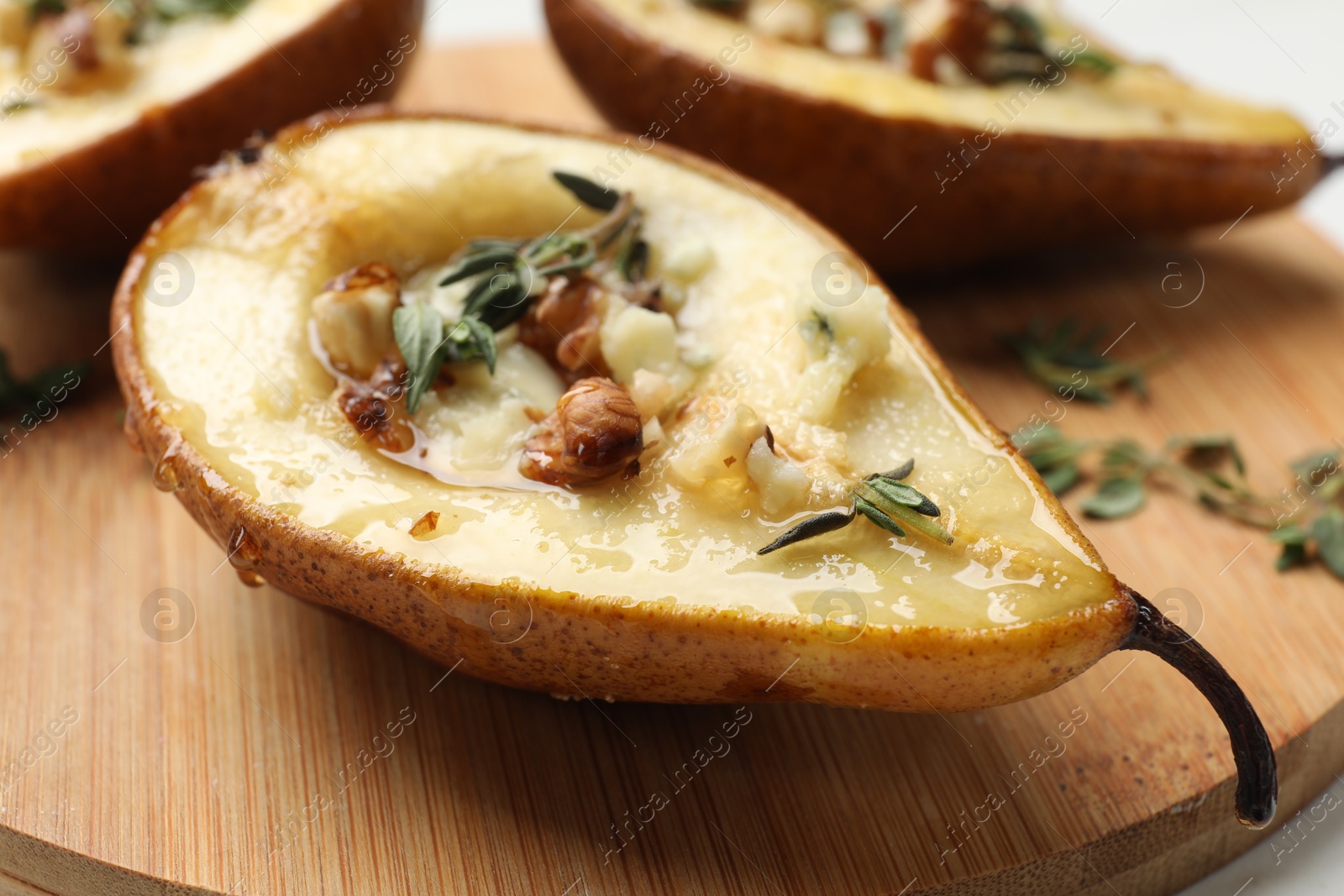 Photo of Tasty baked pears with nuts, blue cheese, thyme and honey on wooden board, closeup