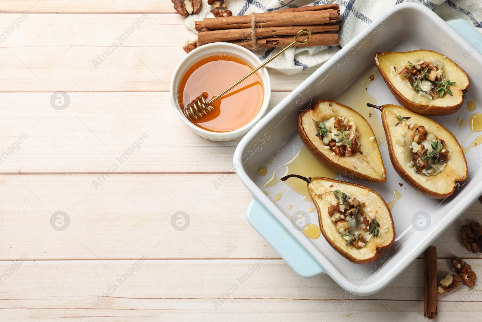 Photo of Tasty baked pears with nuts, blue cheese, thyme and honey in baking dish on wooden table, flat lay. Space for text