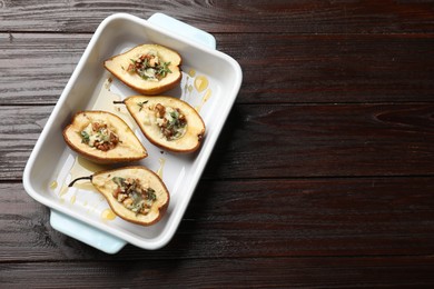 Tasty baked pears with nuts, blue cheese, thyme and honey in baking dish on wooden table, top view. Space for text