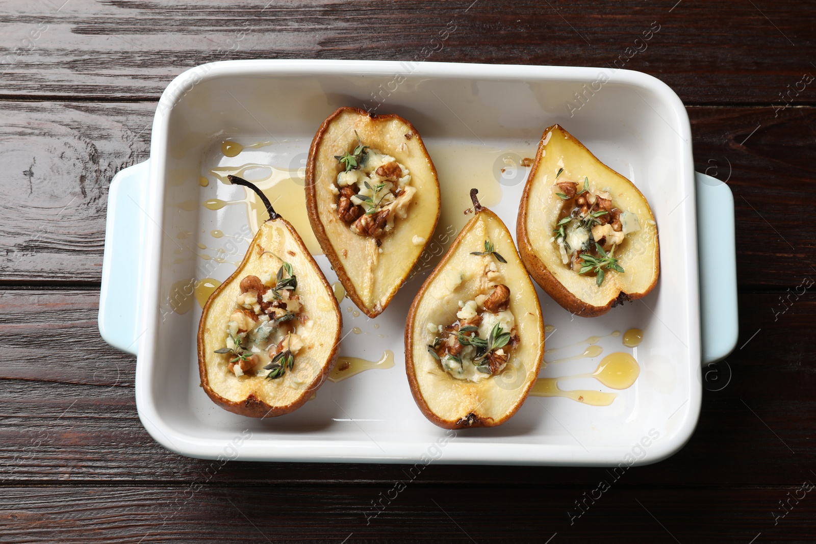 Photo of Tasty baked pears with nuts, blue cheese, thyme and honey in baking dish on wooden table, top view