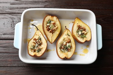 Tasty baked pears with nuts, blue cheese, thyme and honey in baking dish on wooden table, top view