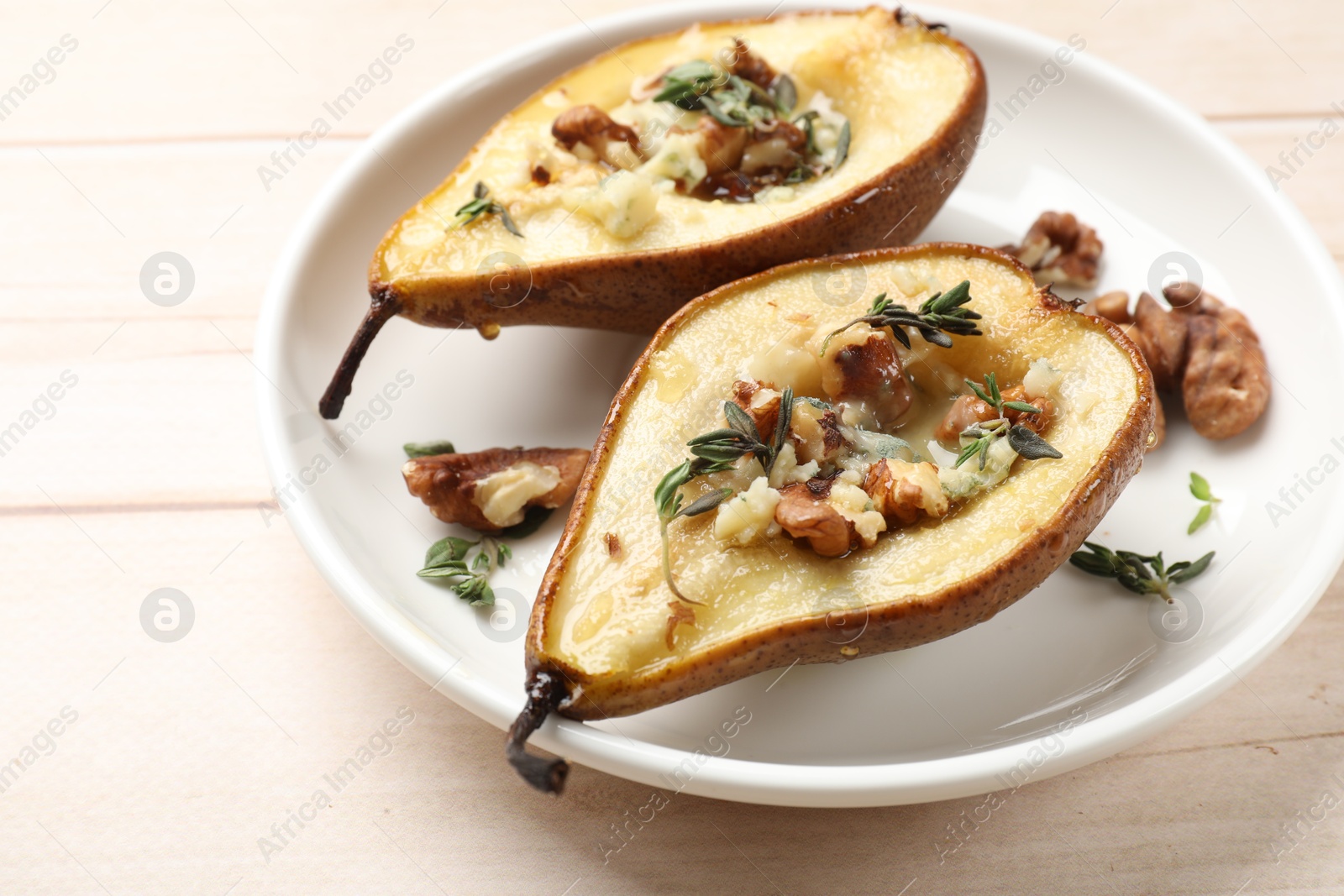 Photo of Tasty baked pears with nuts, blue cheese, thyme and honey on wooden table, closeup