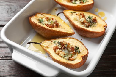 Photo of Tasty baked pears with nuts, blue cheese, thyme and honey in baking dish on wooden table, closeup