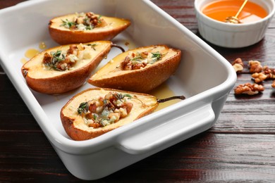 Tasty baked pears with nuts, blue cheese, thyme and honey in baking dish on wooden table, closeup