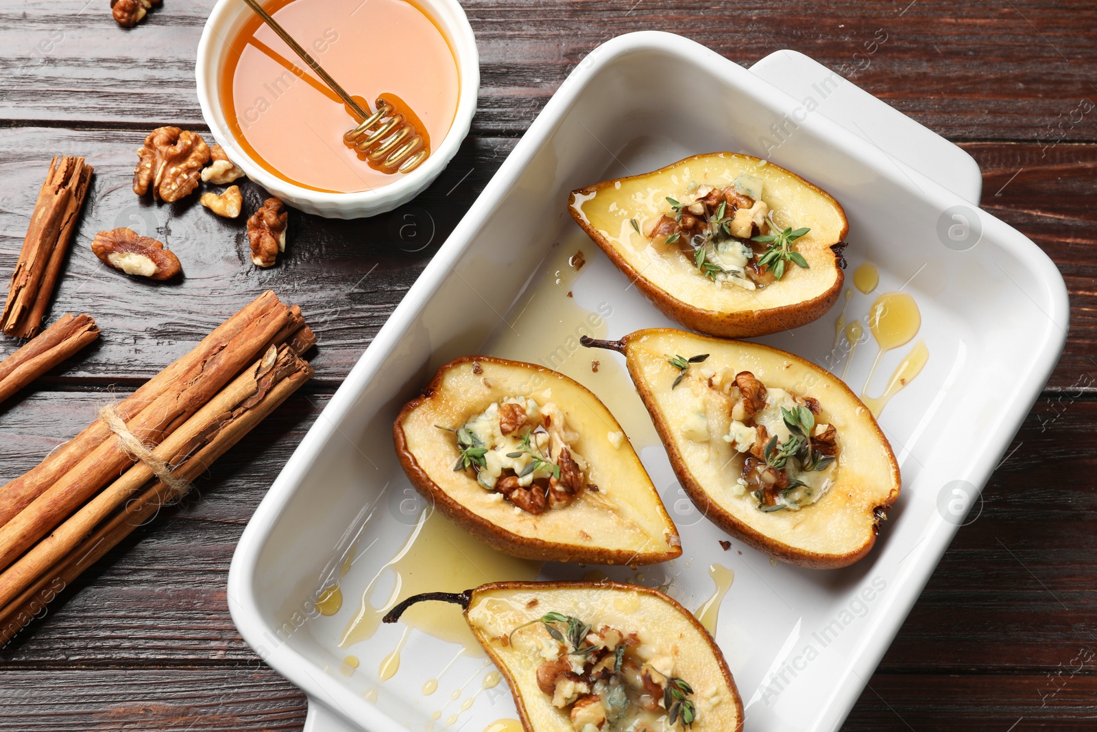 Photo of Tasty baked pears with nuts, blue cheese, thyme and honey in baking dish on wooden table, flat lay