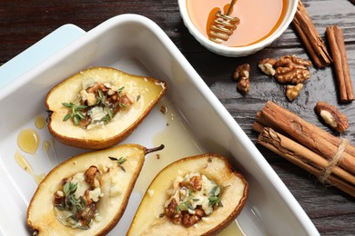 Tasty baked pears with nuts, blue cheese, thyme and honey in baking dish on wooden table, flat lay