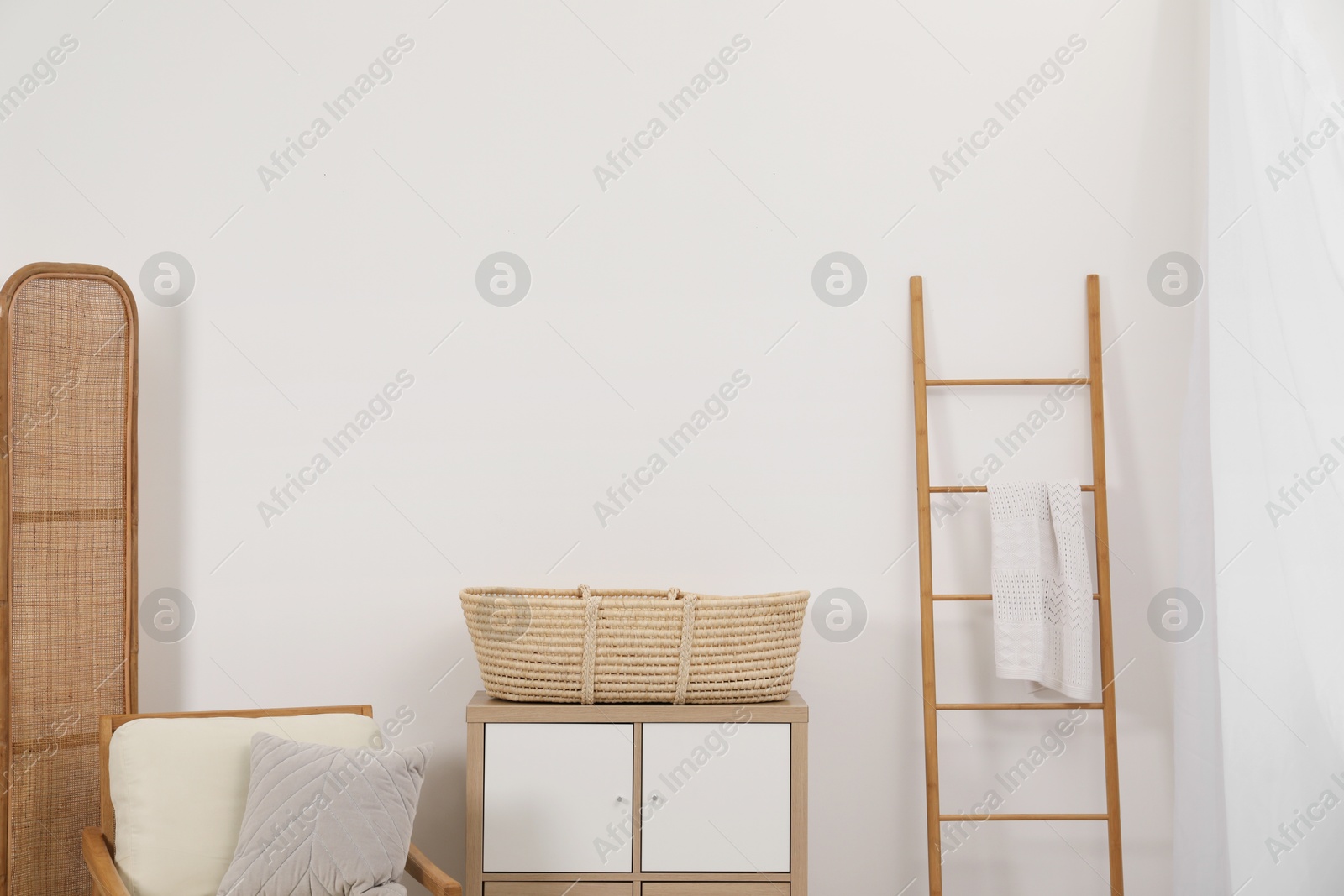 Photo of Armchair with cushion, wicker basket on nightstand and wooden ladder in room