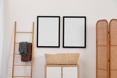 Photo of Empty frames hanging on wall, wicker basket and wooden ladder in room