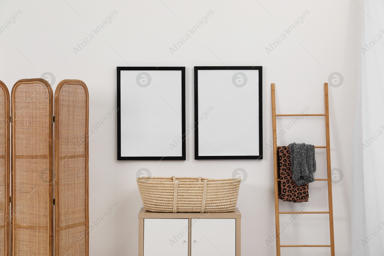 Photo of Empty frames hanging on wall, wicker basket and wooden ladder in room