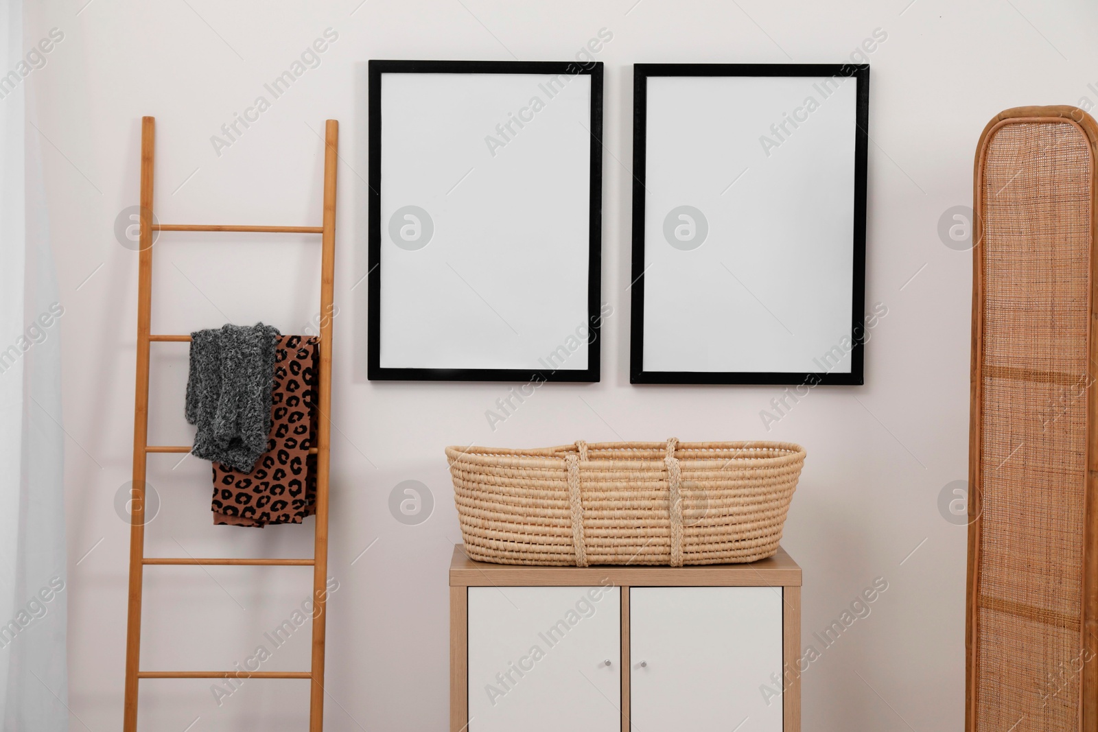 Photo of Empty frames hanging on wall, wicker basket and wooden ladder in room