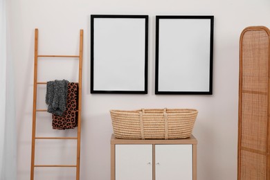 Empty frames hanging on wall, wicker basket and wooden ladder in room