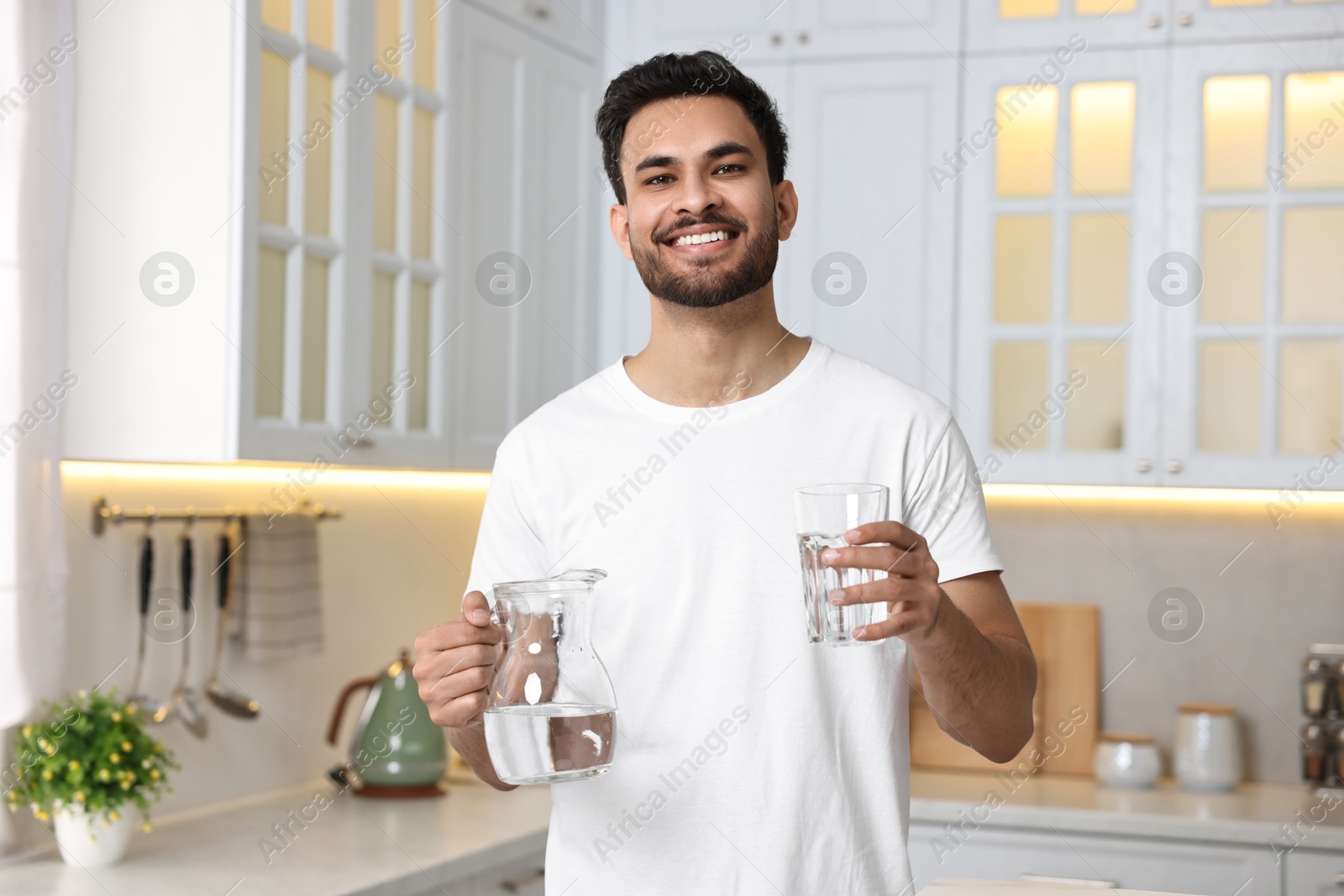 Photo of Happy man with jug and glass of water in kitchen at morning